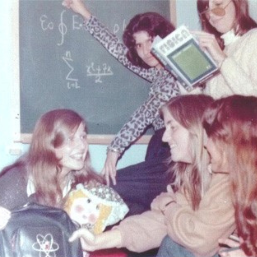 Marcia jovem, com quatro amigas, olhando livros de física e escrevendo em um quadro negro.